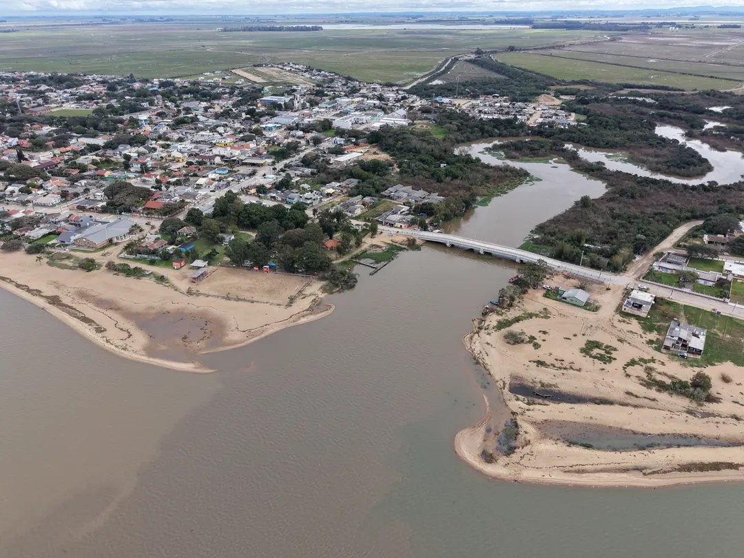 Foz do arroio encontrando a Lagoa dos Patos, com bancos de areia e a ponte ao fundo, em Arambaré